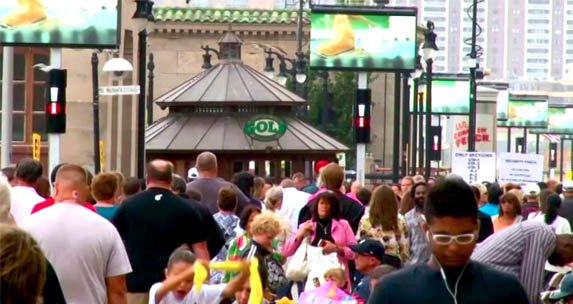 Boardwalk visitors passing an APM digital screen in daylight